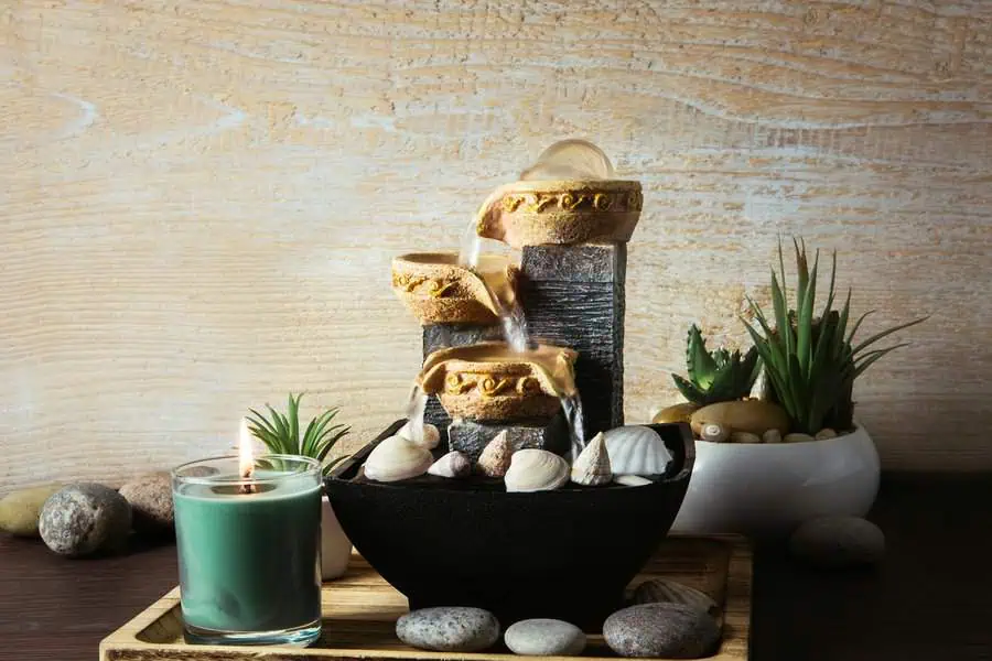 Desk setup with a small water fountain, rocks, plants, and a lit candle for a peaceful, feng shui-inspired atmosphere.