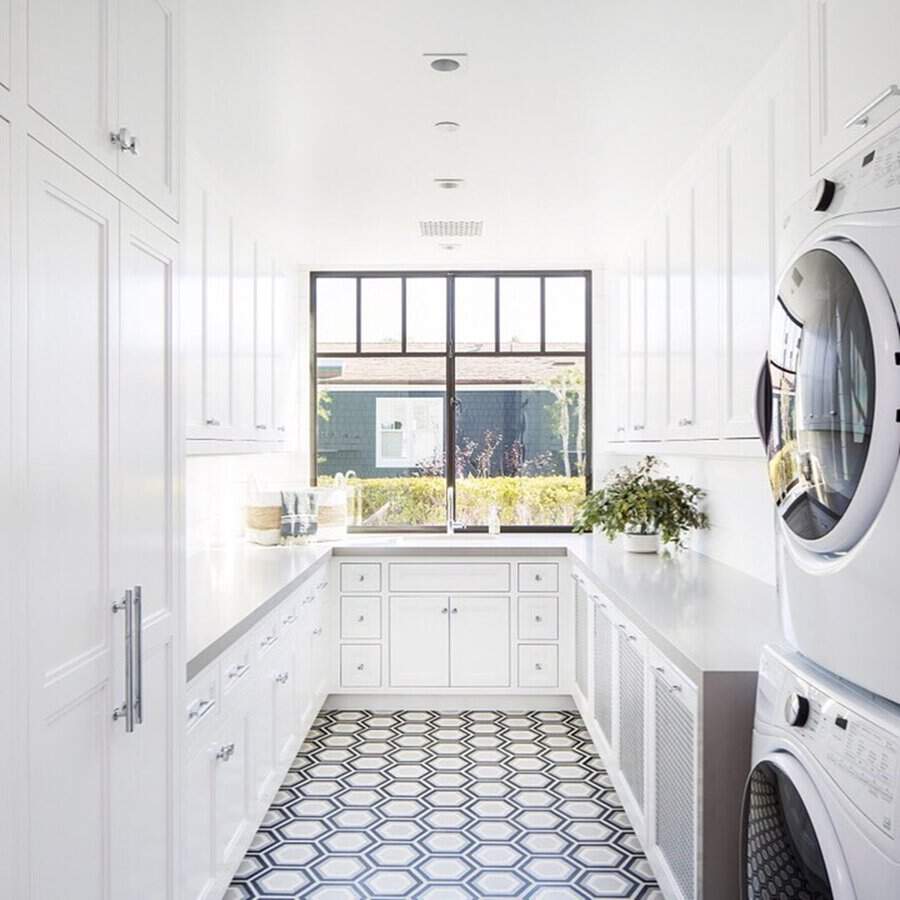 Bright white laundry room with stacked washer and dryer, large window, black frame, and hex tile floor.
