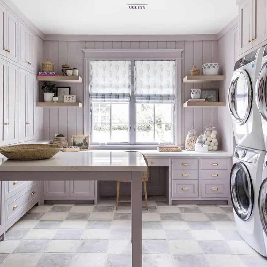 Lavender laundry room with paneled walls, built-in cabinets, a center table, and stacked washer-dryer near large windows.
