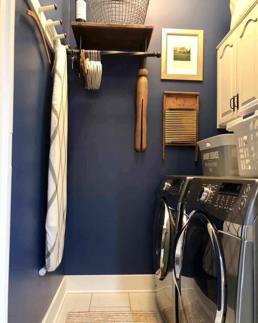 Laundry room with navy walls, front-loading washer, wooden shelf, vintage accents, and an ironing board on the side.
