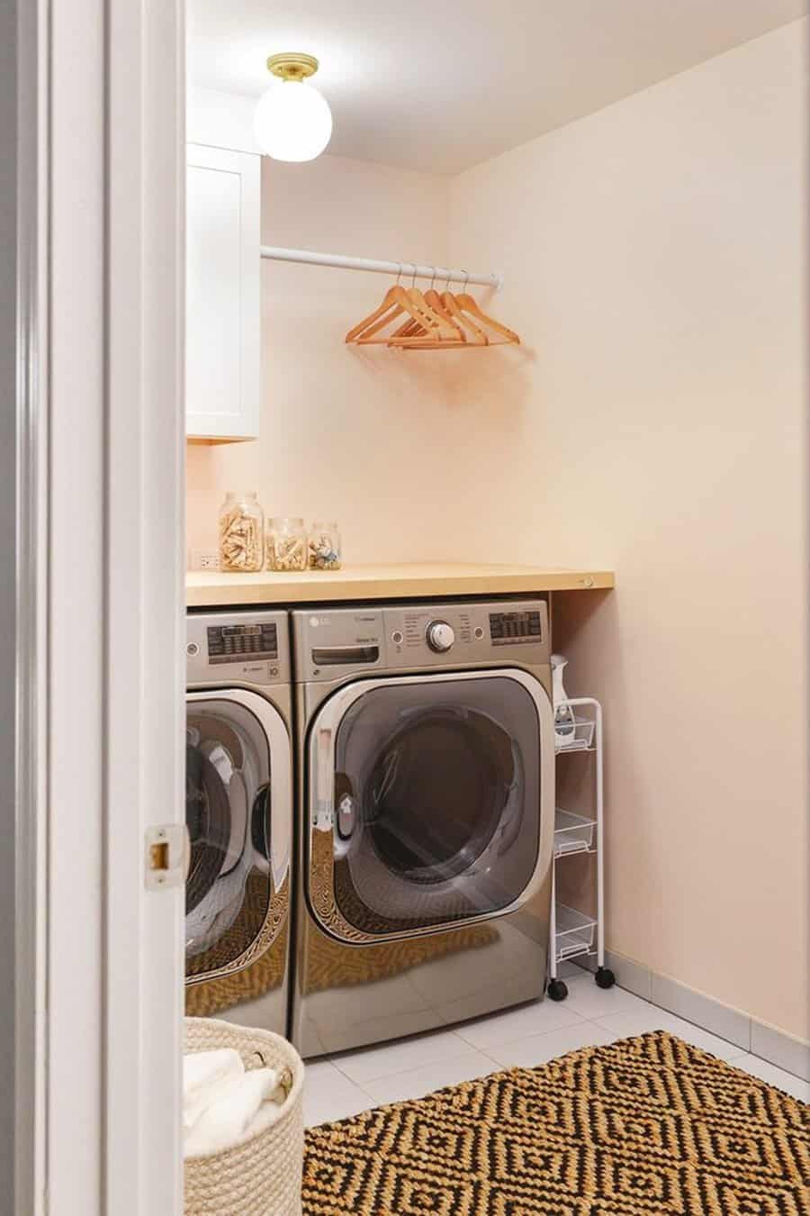 Peach laundry room with front-loading machines, a small folding countertop, and a patterned rug for a cozy, functional space.