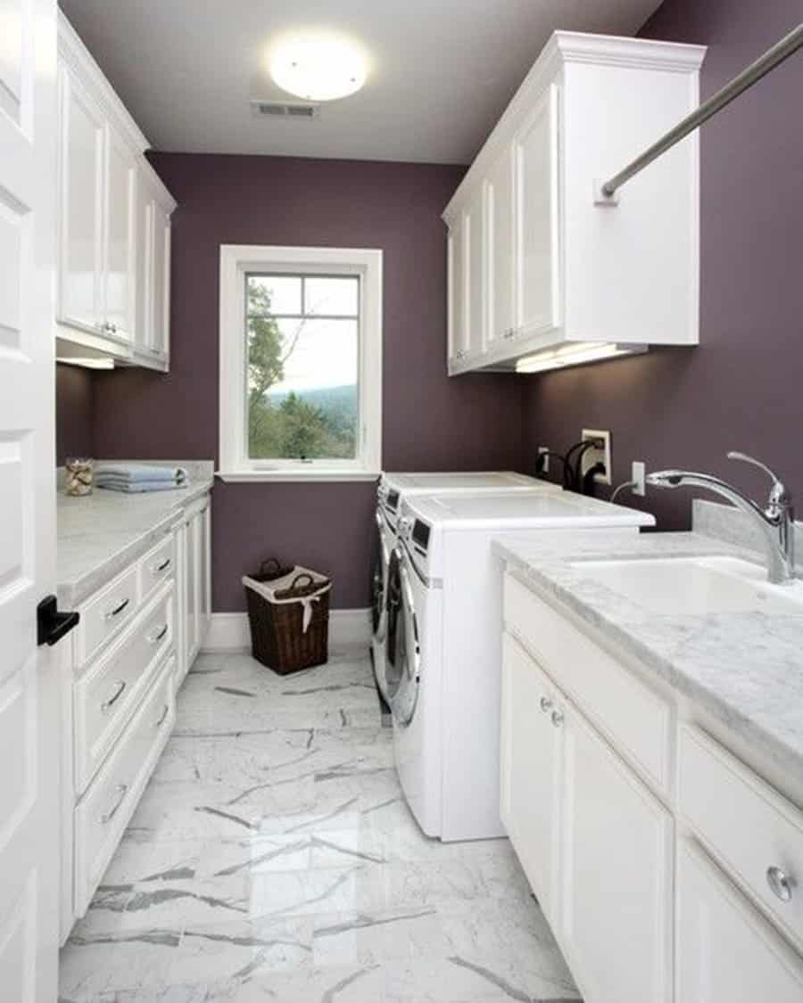 Purple laundry room with white cabinets, marble floors, front-loading appliances, and a window view.