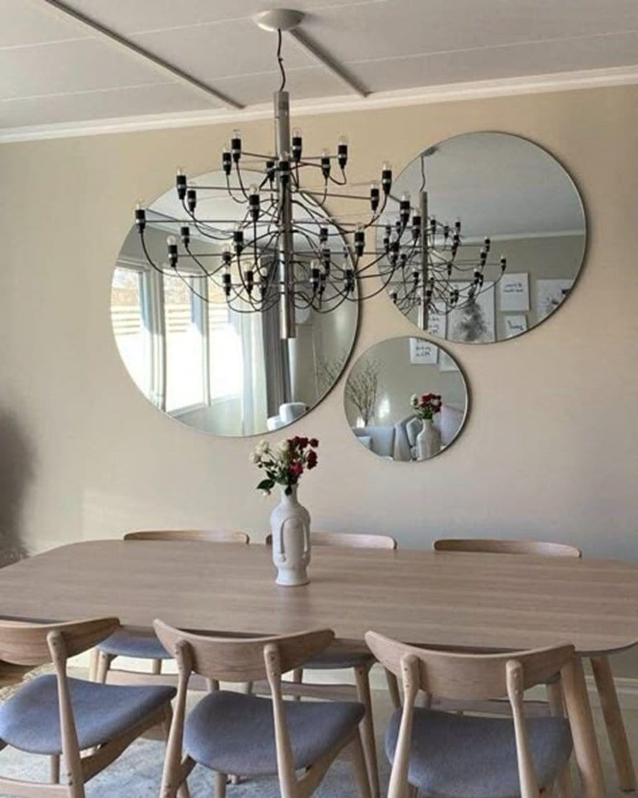 Group of round mirrors above a dining table, reflecting a chandelier and adding style to the minimalist dining room.