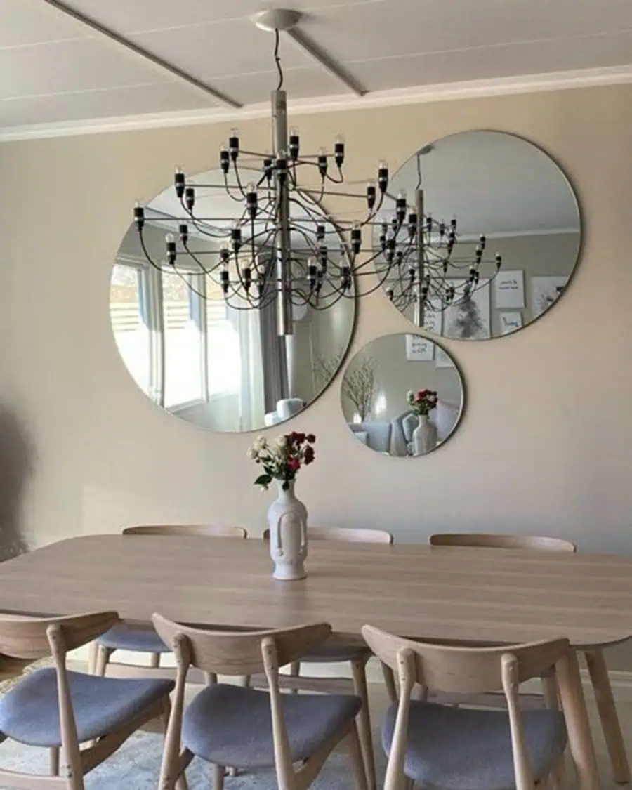 Group of round mirrors above a dining table, reflecting a chandelier and adding style to the minimalist dining room.