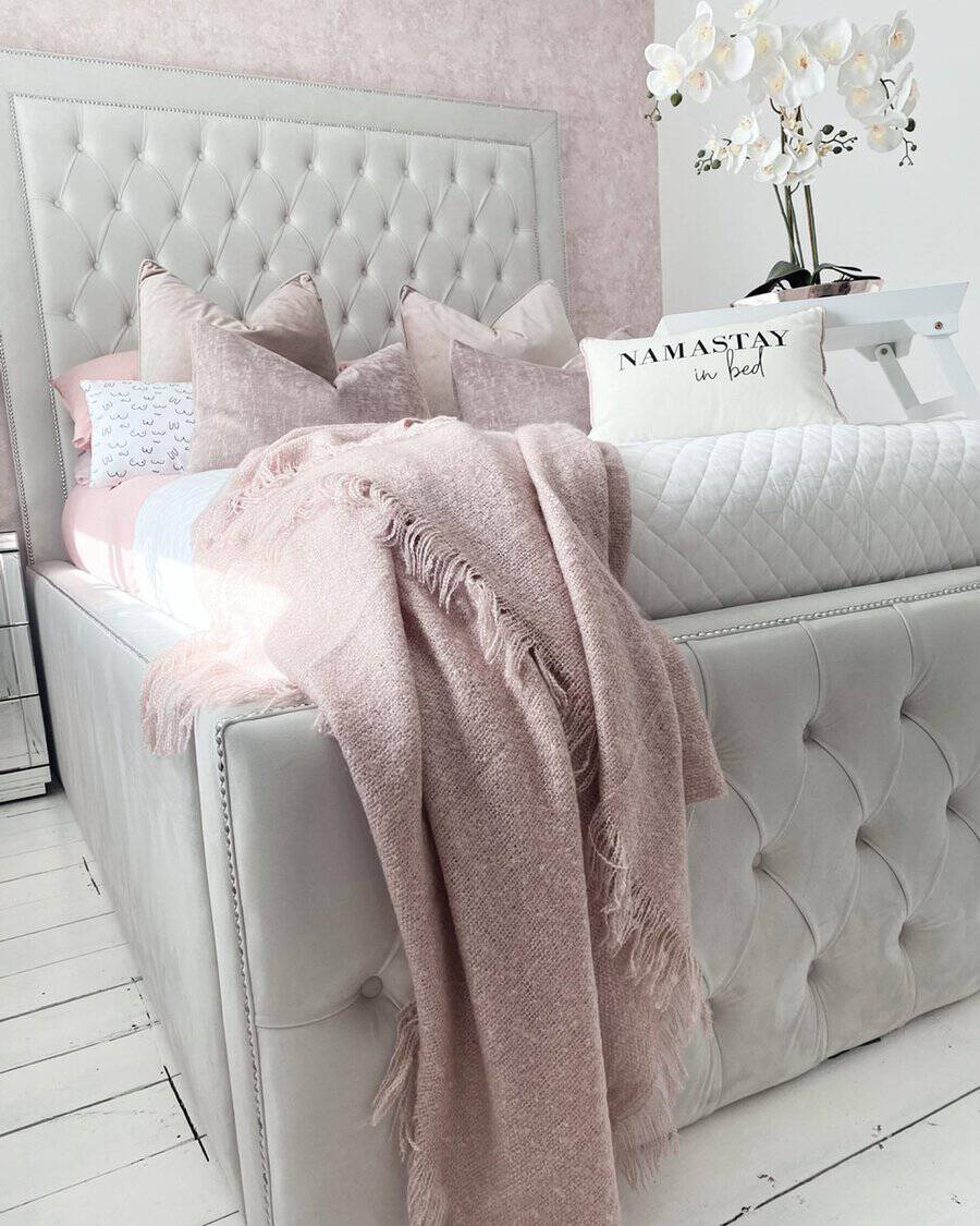 Layered textiles with a soft pink throw, quilted bedding, and plush pillows create a cozy and elegant bedroom retreat.