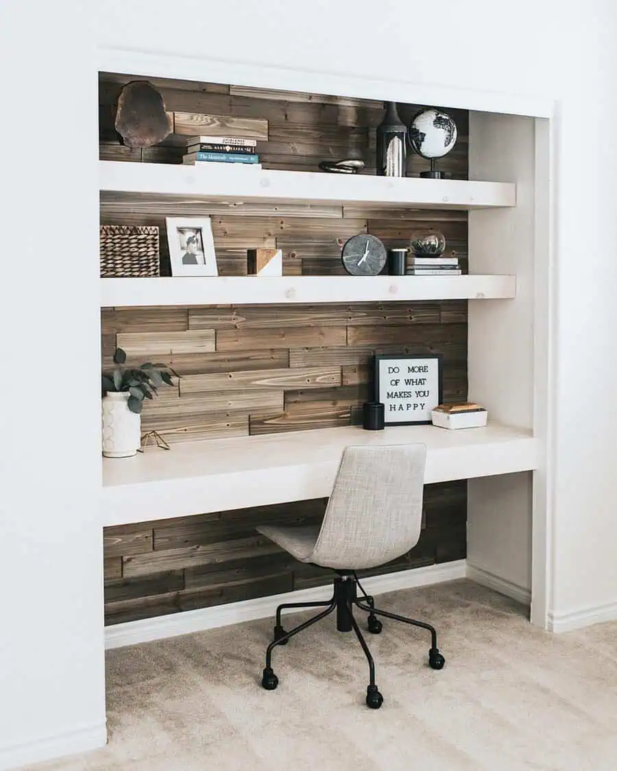Closet office with a wood accent wall, floating shelves, a built-in desk, and a neutral upholstered chair in a modern rustic design.