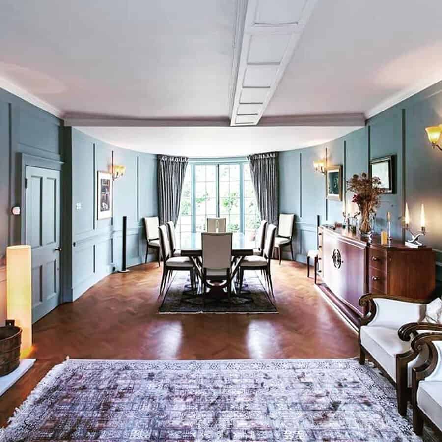 Georgian-style dining room with blue paneled walls, bay window, and modern furnishings on warm wood floors.