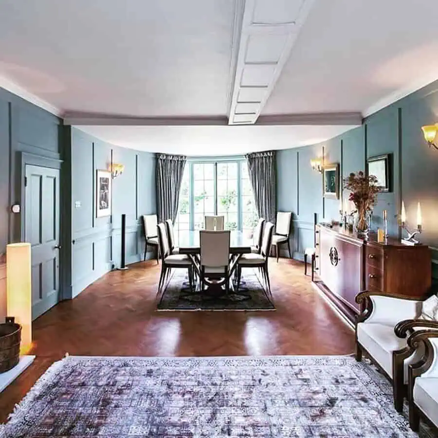 Georgian-style dining room with blue paneled walls, bay window, and modern furnishings on warm wood floors.