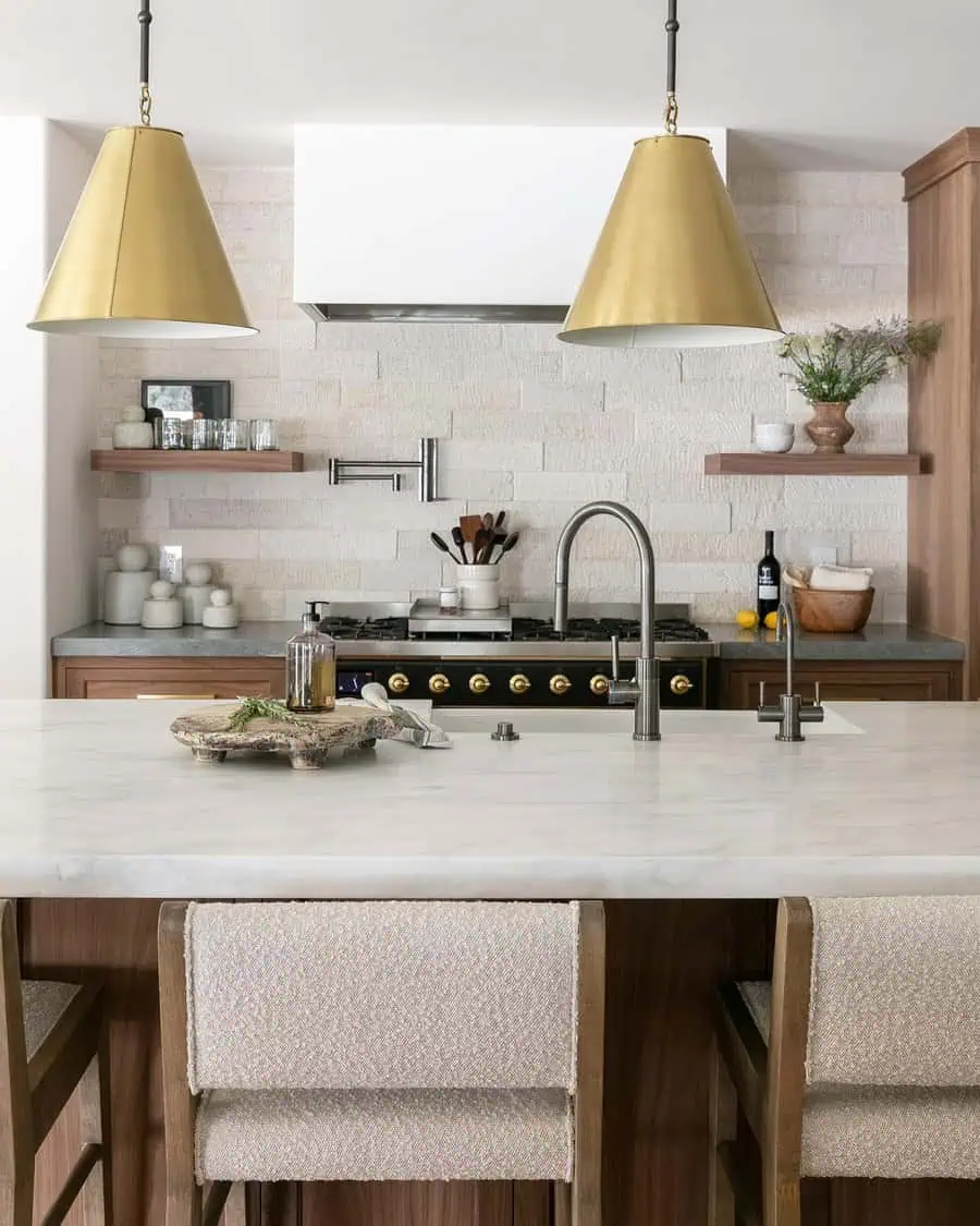 Spanish-inspired kitchen with a light stone backsplash, wood cabinetry, brass pendant lights, a marble island, and a black range with gold details.
