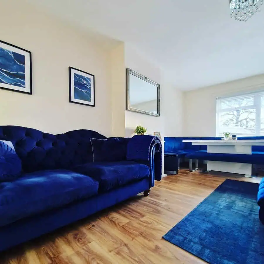 Living room with a navy velvet sofa, matching banquette, wood floors, and a large mirror brightening the space.