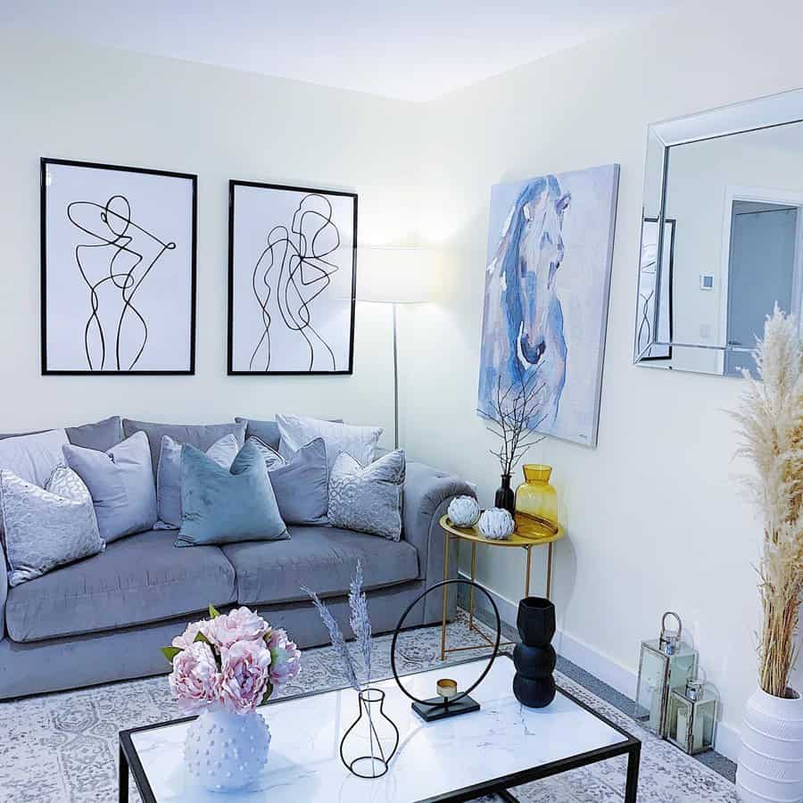 Light living room with line-art prints, a blue horse painting, gray sofa, mirrored accents, and layered pillows for a cozy, modern feel.