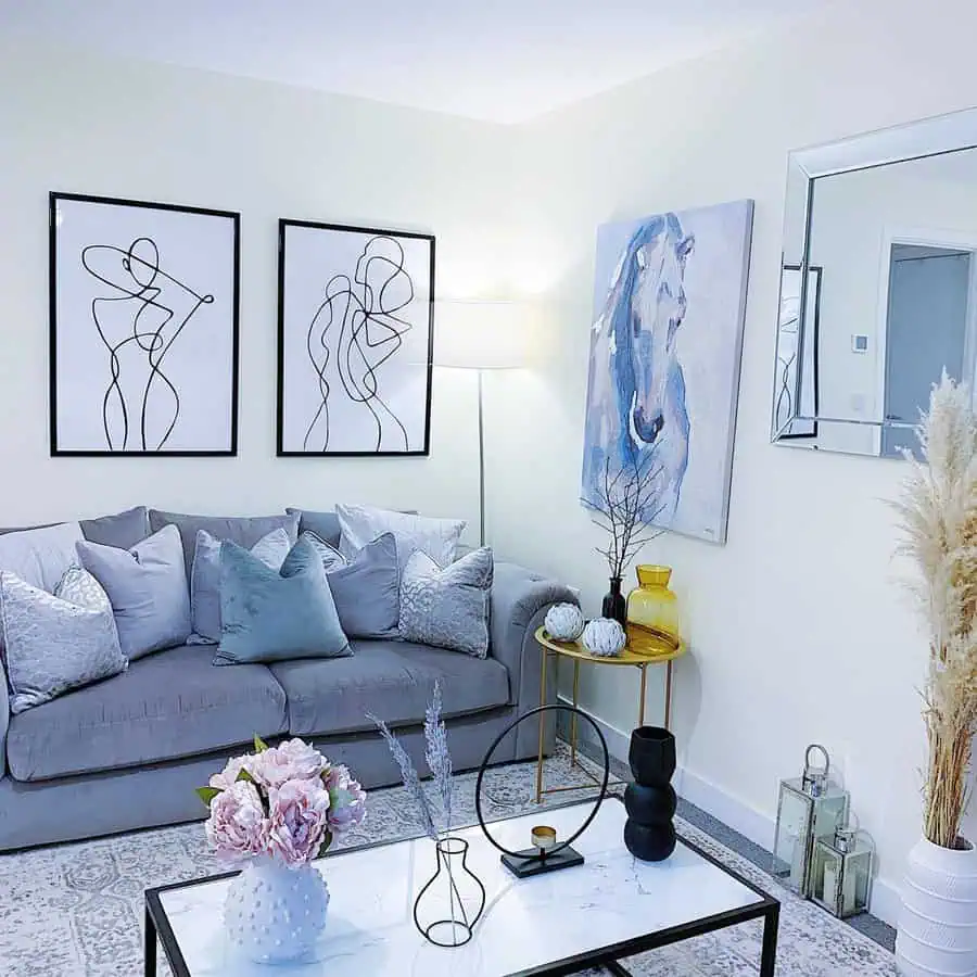 Light living room with line-art prints, a blue horse painting, gray sofa, mirrored accents, and layered pillows for a cozy, modern feel.