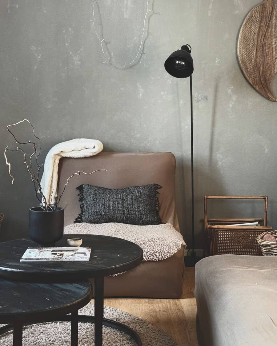 Corner with a brown lounge chair, black lamp, muted walls, round tables, and layered throws for cozy texture.