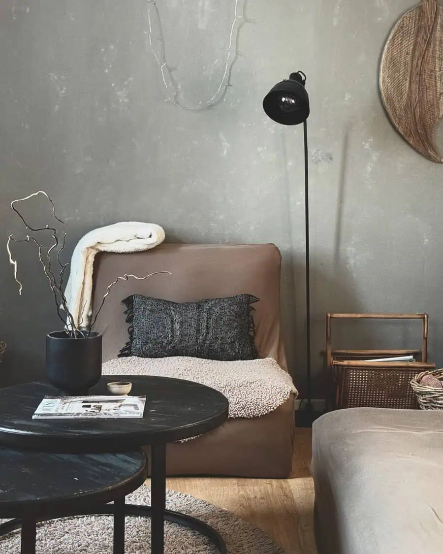 Corner with a brown lounge chair, black lamp, muted walls, round tables, and layered throws for cozy texture.