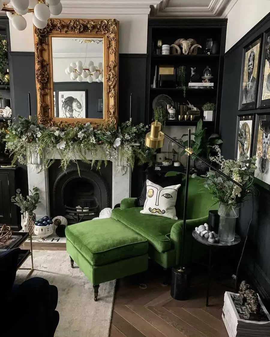Dark living room with a gold mirror over the fireplace, black walls, and a green velvet chaise adding bold contrast.