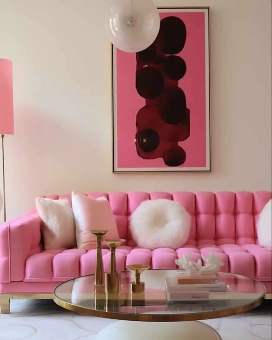 Living room featuring a bright pink tufted sofa, matching abstract art, gold accents, and a glass coffee table for a glam look.