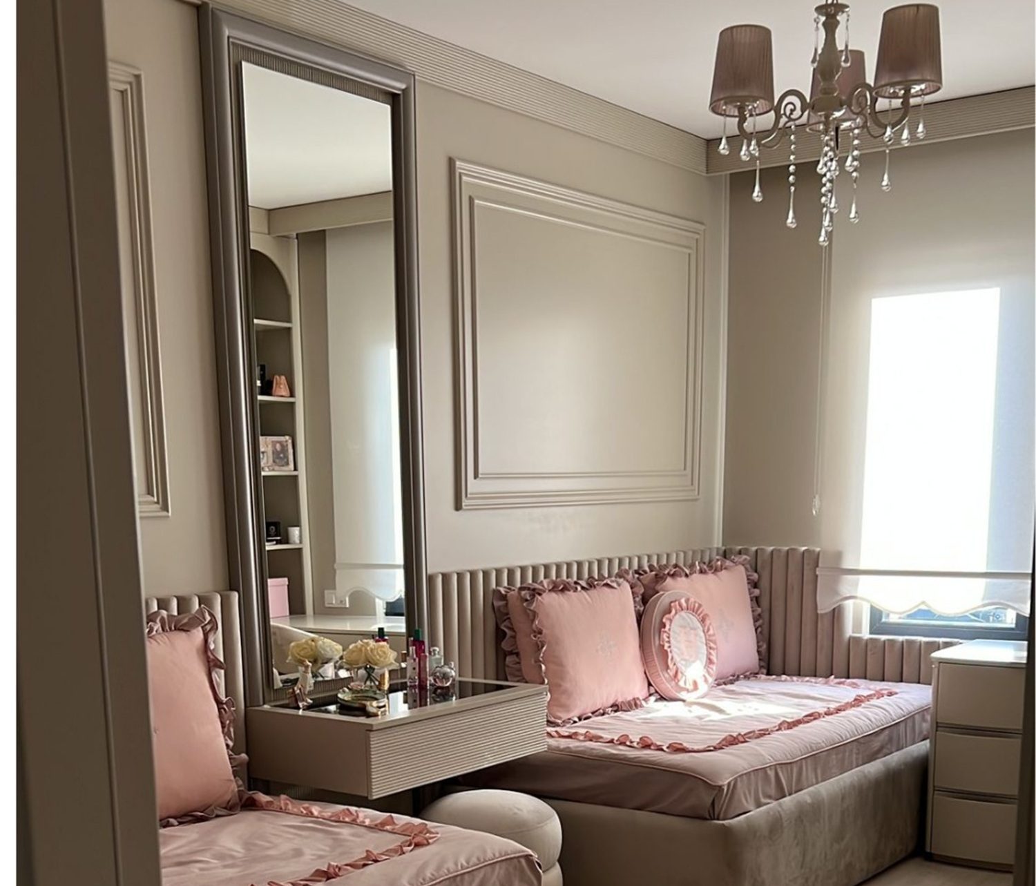 Serene bedroom with neutral walls, a tall mirror, tufted blush seating, and a chandelier adding a soft, romantic feel.