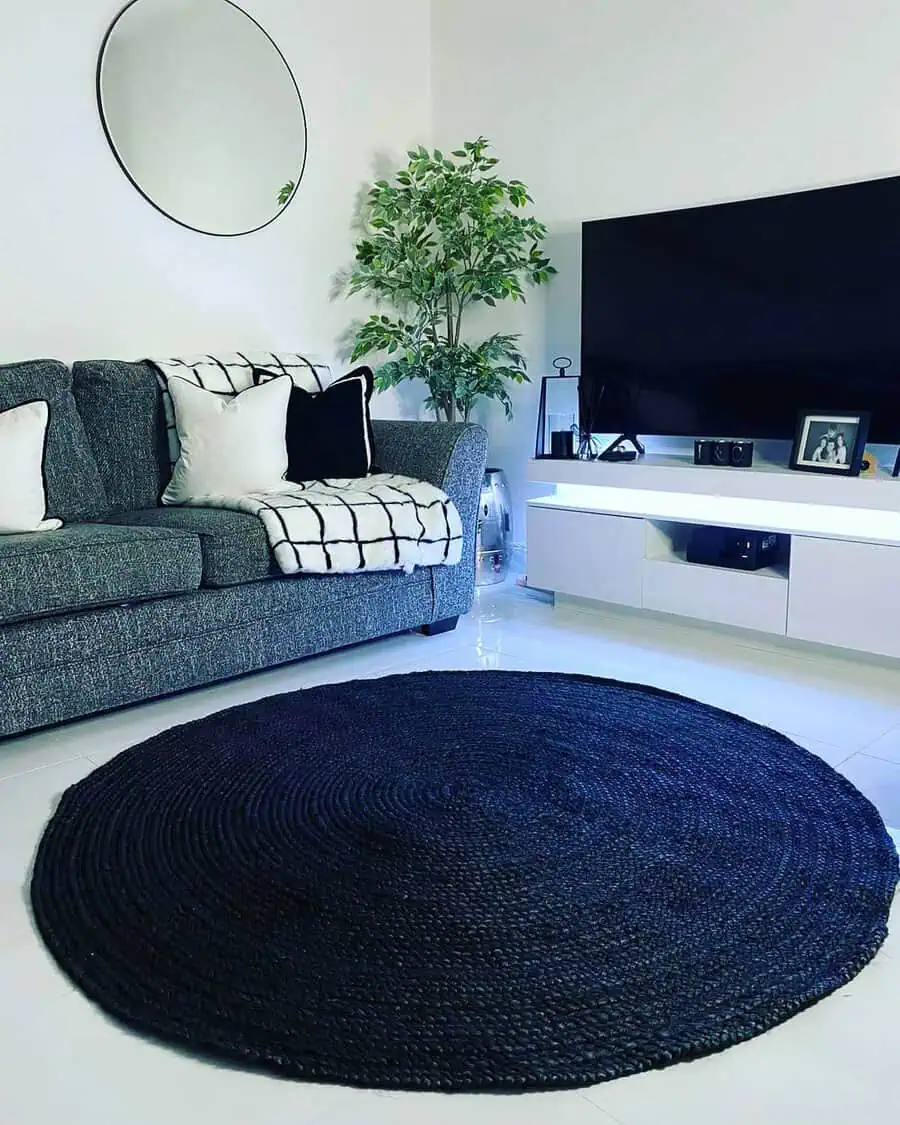 Living room with a round black rug, gray sofa, and white TV stand, creating a bold monochrome contrast.