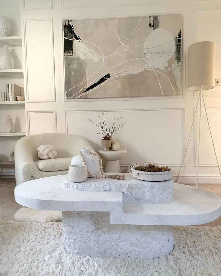White sculptural coffee table, boucle chair, and abstract art in a neutral-toned living area with panelled walls.