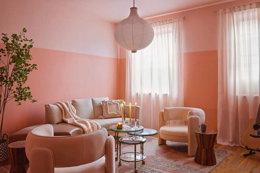 Peach two-tone living room with neutral seating, sheer curtains, and a low glass table creating a soft, welcoming space.
