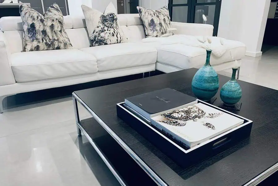 White sofa with monochrome pillows, teal vases on a black coffee table, adding a bold color pop in a sleek, modern living room.