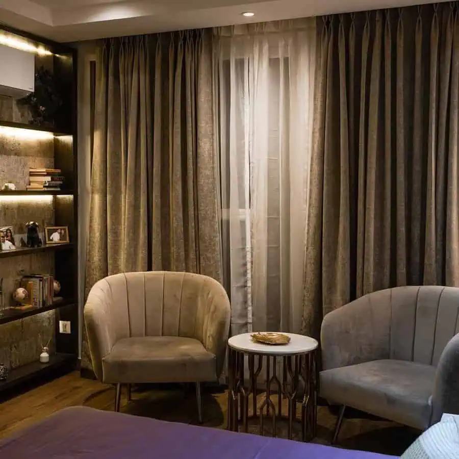 Monochrome bedroom sitting area with neutral velvet chairs, a marble-top table, and textured drapes for a refined, cohesive look.