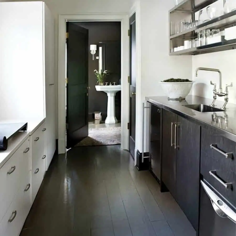 Kitchen-laundry space with charcoal wood floor, white cabinetry, stainless counters, and a dark door.