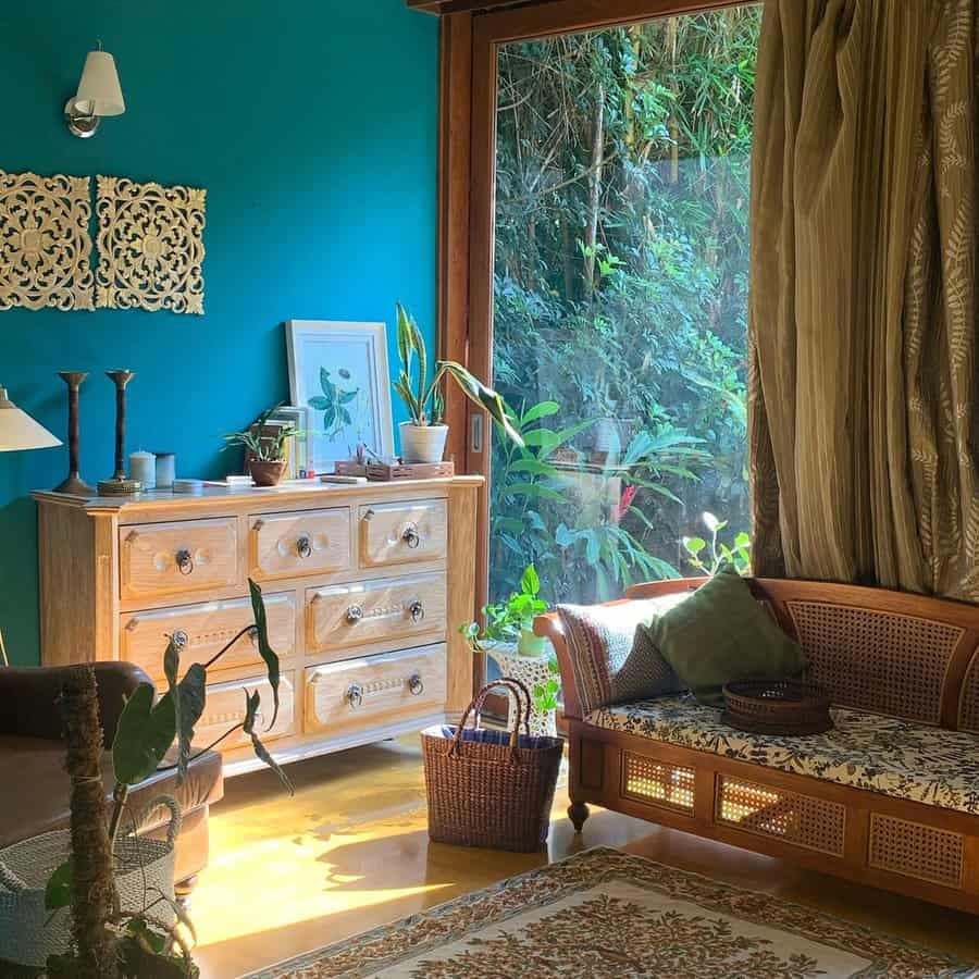 Bedroom sitting area with a rattan daybed, green walls, large windows, wooden furniture, and botanical decor for a natural, earthy feel.