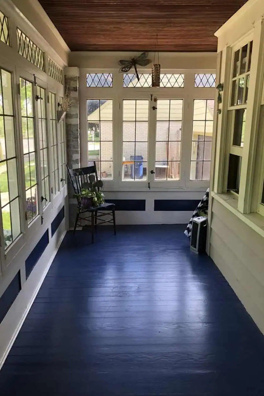 Bright porch with navy-painted floor, wooden ceiling, leaded windows, and a simple rocking chair.