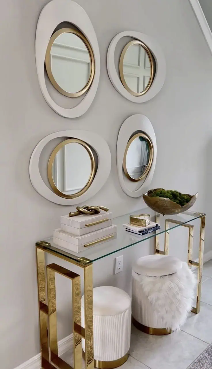 Group of circular mirrors with gold frames above a modern console table with decorative accessories and plush stools.