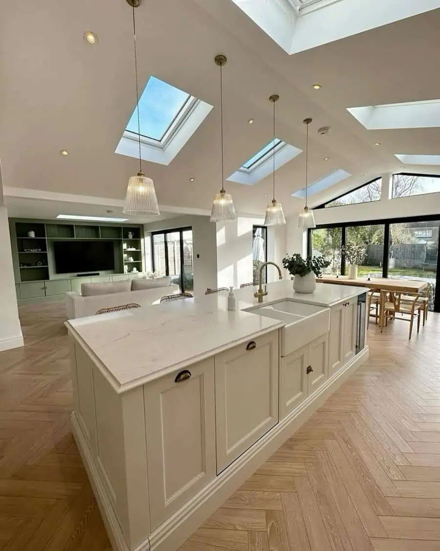 Open-concept kitchen with several skylights, farmhouse sink island, clear pendants, and herringbone wood flooring.