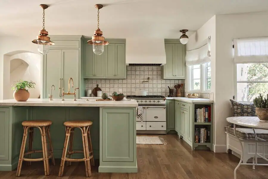 Spanish-style kitchen with sage green cabinets, copper lighting, a tile backsplash, woven barstools, and a cozy breakfast nook.
