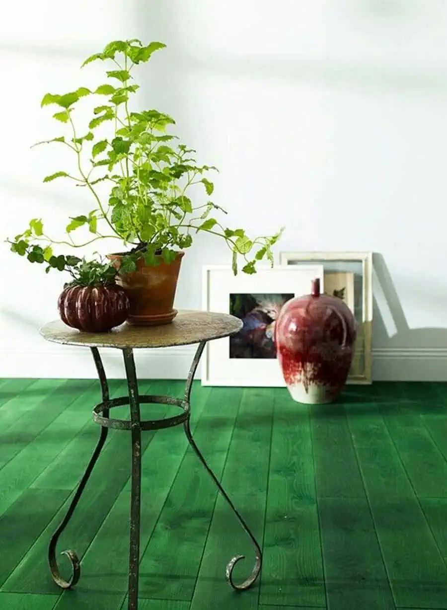 Wood floor painted bright green, featuring a small metal table with potted plants and decorative accents.