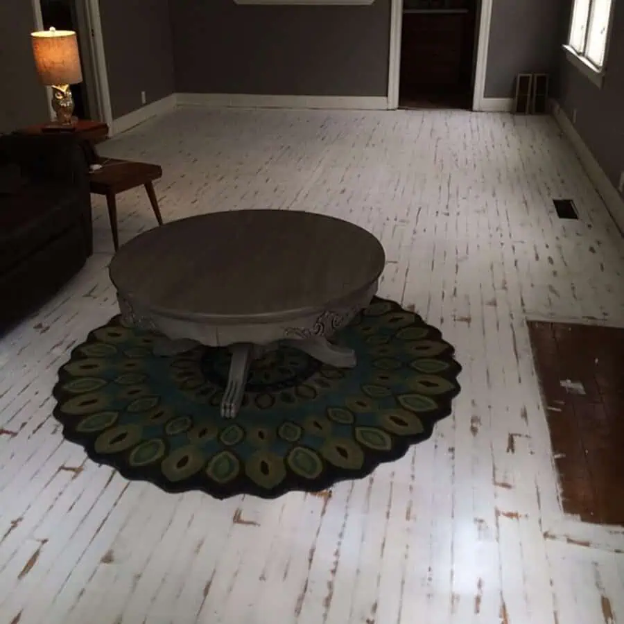 Living room with distressed white painted floor, dark walls, a round coffee table, and a peacock-inspired rug at the center.
