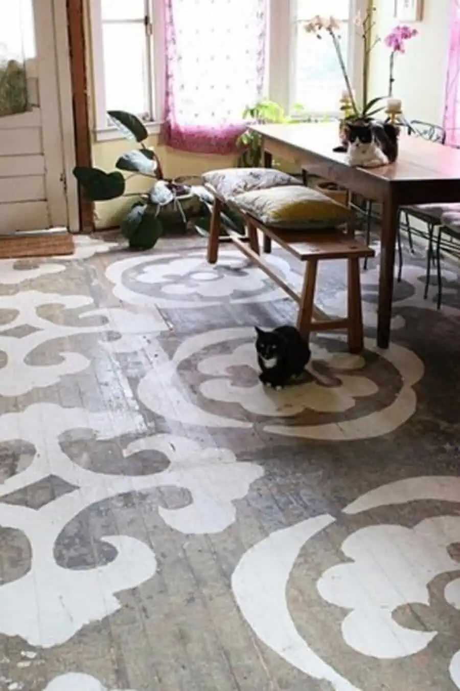 Distressed wood floor with white stenciled floral design, rustic furniture, and two black-and-white cats lounging nearby.