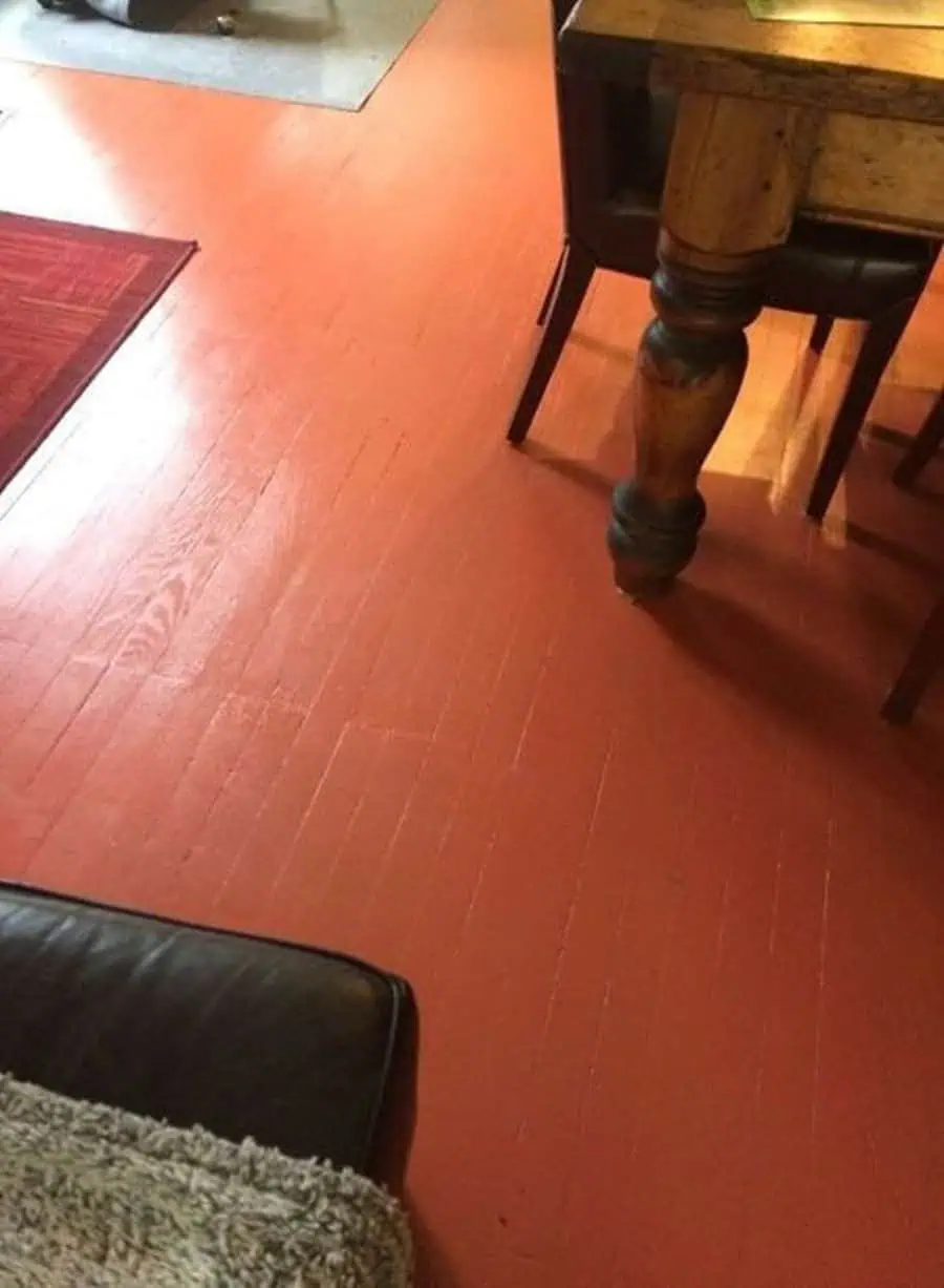 Terracotta-painted wood floor in a dining area with a rustic table and chair.
