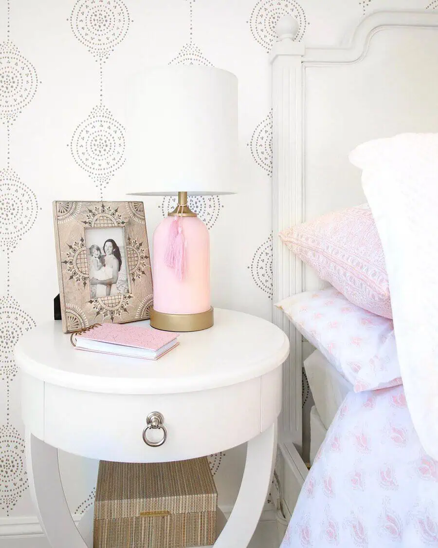 Chic pastel pink lamp with gold accents and a tassel detail adds warmth and elegance to a stylish bedside table.