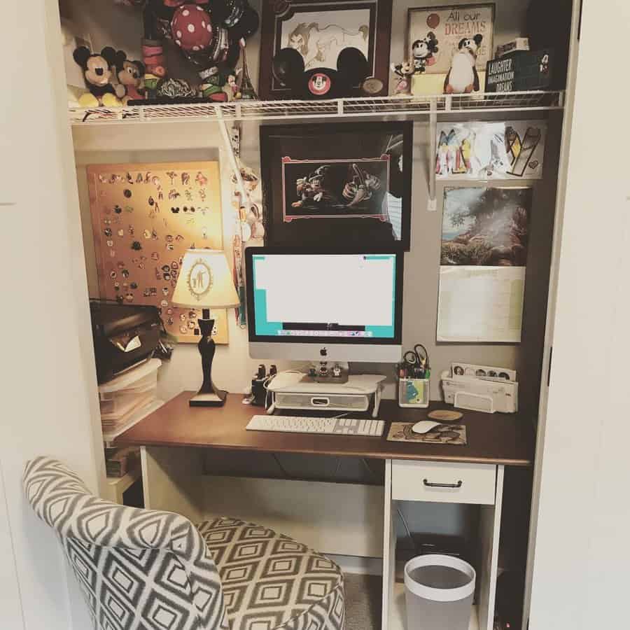 Closet office with Disney-themed decor, framed artwork, a corkboard, collectibles, a wooden desk, and a patterned upholstered chair.