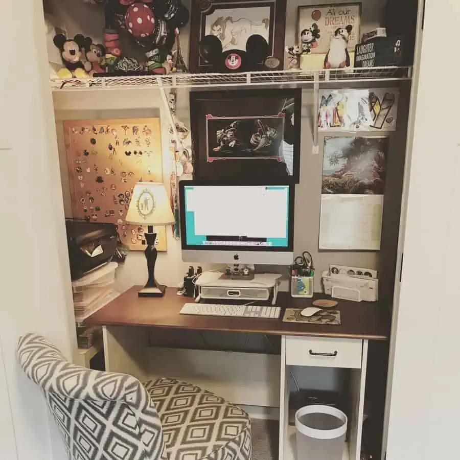Closet office with Disney-themed decor, framed artwork, a corkboard, collectibles, a wooden desk, and a patterned upholstered chair.