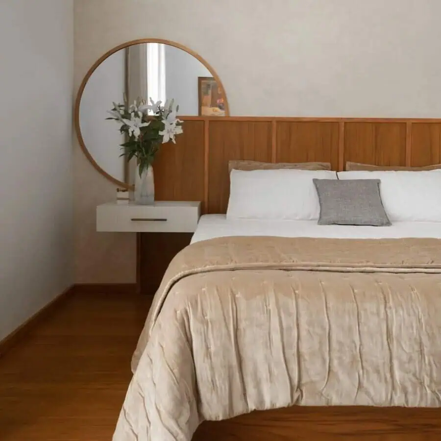Round mirror above a nightstand with lilies in a vase, complementing a minimalist bedroom with a wood headboard and neutral bedding.