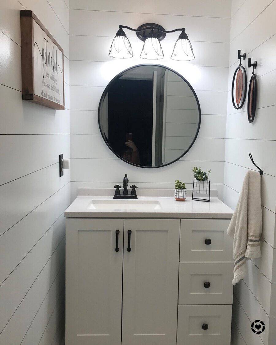 Stylish round mirror and minimalist decor in a bright bathroom with light fixture, sink, and small plants.