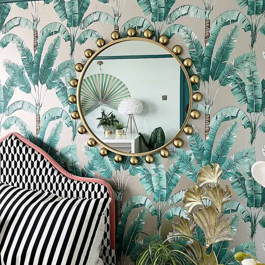 Round mirror with golden accents above a bed, set against tropical palm leaf wallpaper and geometric patterns in a stylish bedroom.