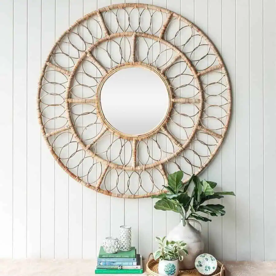 Woven mirror above a table with plants, books, and decorative items against a light paneled wall.
