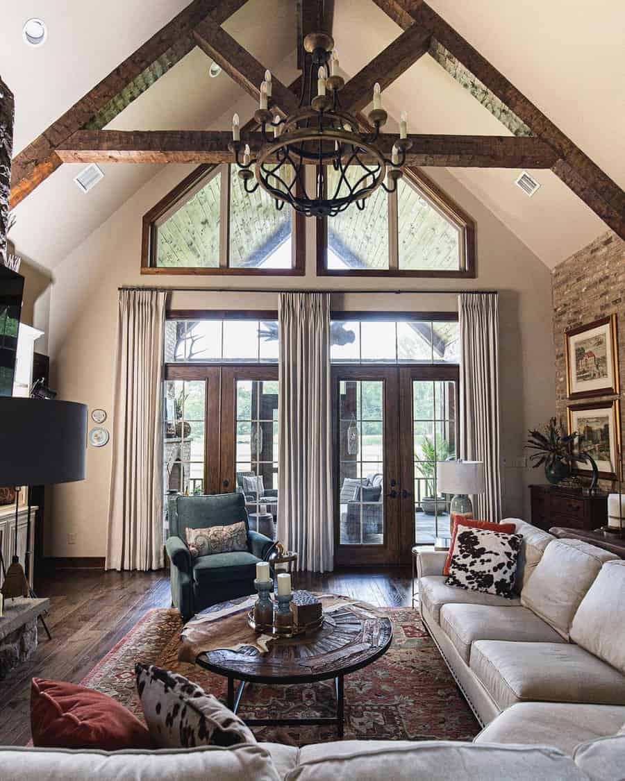 Living room with exposed wood trusses, large chandelier, neutral seating, and French doors revealing an outdoor view.