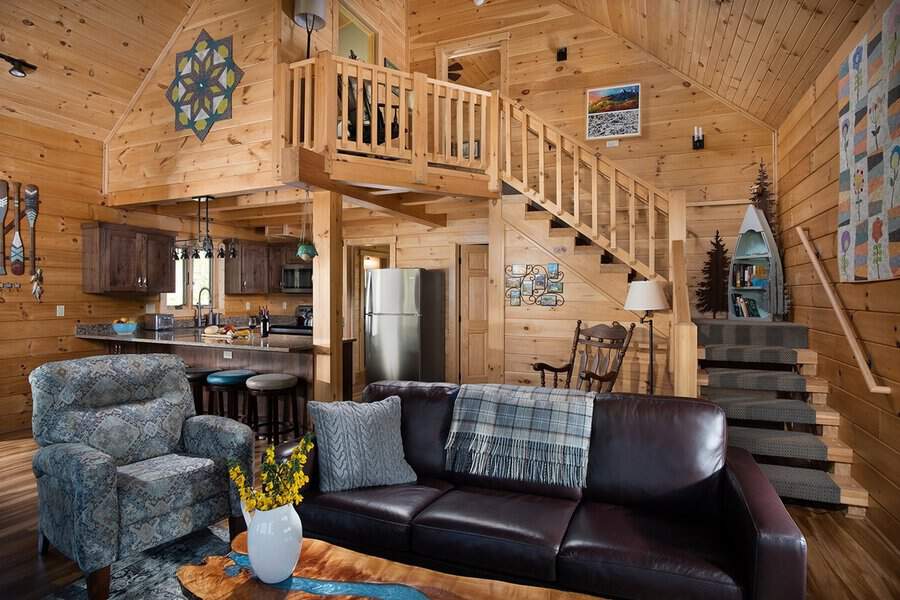 Cozy pine cabin with a tall wood ceiling, lofted nook, open kitchen, and comfy seating in a warm, rustic living space.