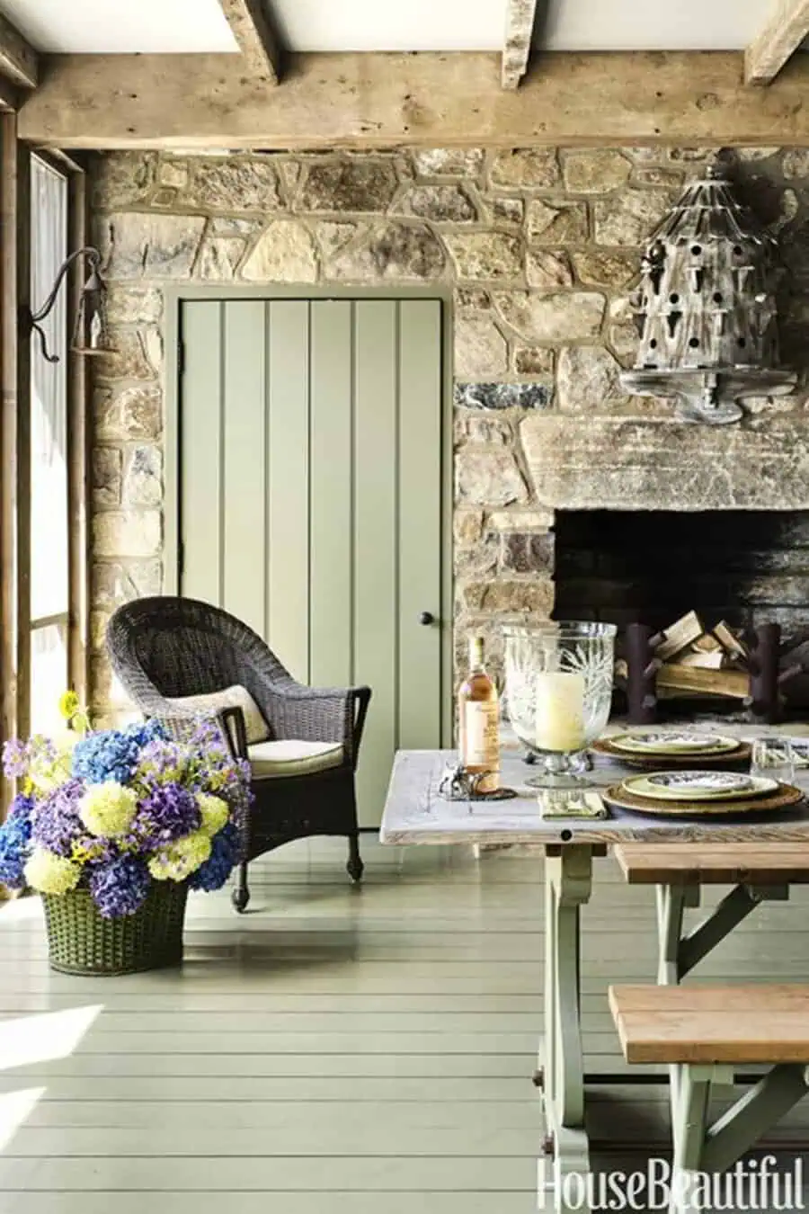 Rustic room with sage green painted floor, matching door, stone fireplace, and a wicker chair.