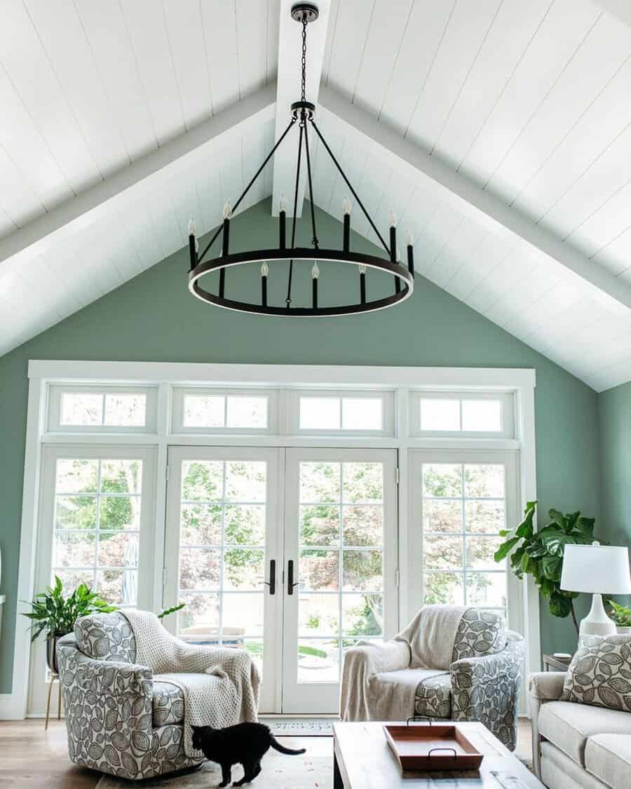 Living room with white shiplap cathedral ceiling, green walls, large windows, and a round chandelier.