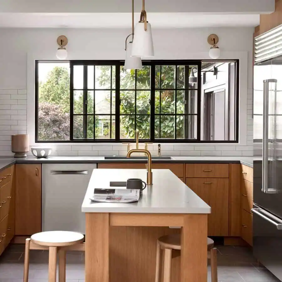 Modern kitchen with black-framed window, warm wood cabinets, and brass fixtures over a streamlined gray countertop.