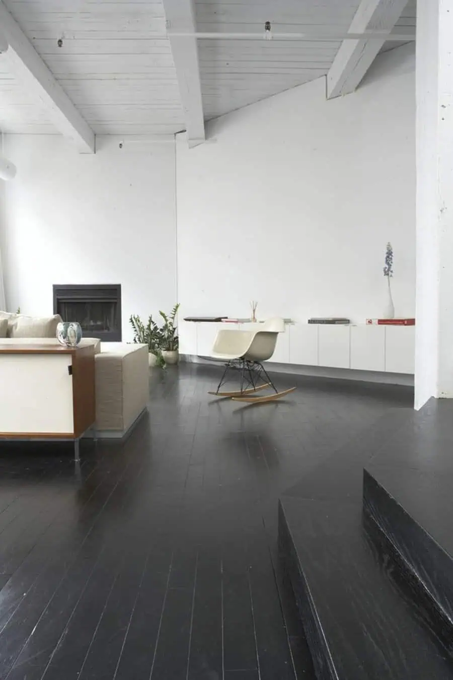 Living room with black painted floor, white walls and ceiling beams, and modern furnishings for dramatic contrast.