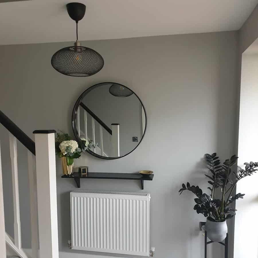 Round mirror and minimalist decor in a stylish entryway with modern lighting, plants, and a black shelf.